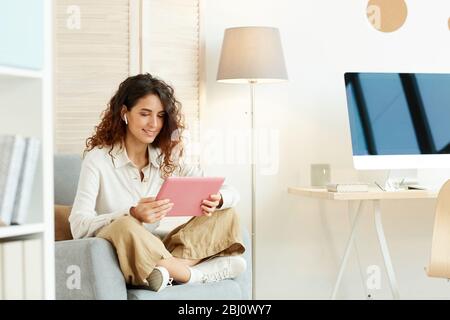 Young woman sitting relaxed in her armchair and working using tablet computer and Internet Stock Photo