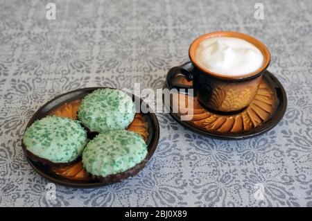 Clay cup of coffee with green marshmallows on the kitchen table. Stock Photo