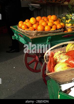 Green and red painted market handcart full of oranges in the market at Menton, south of France - Stock Photo