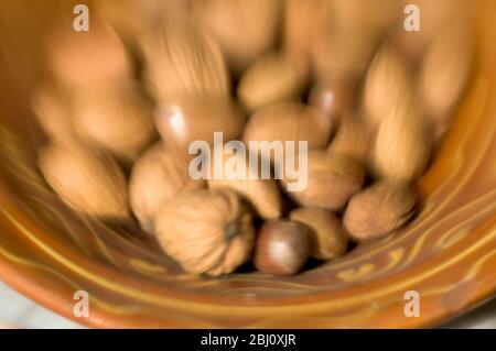 Brown earthenware ceramic bowl of mixed nuts in their shells. Shot with lensbabies lens - Stock Photo