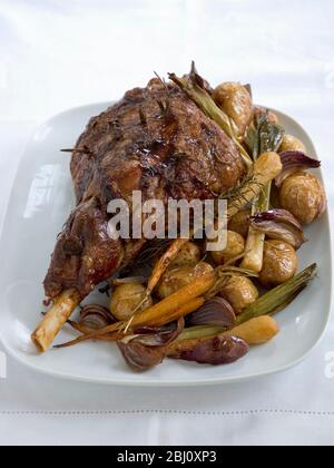 Leg of lamb on serving platter with roast new potatoes in their skins. -