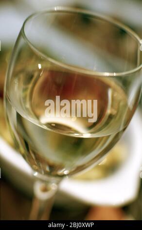 Close up of glass of white wine with dishes of food behind - - Stock Photo
