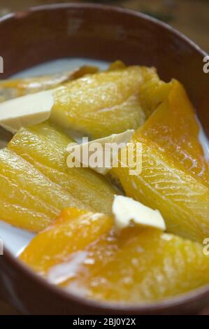 Pieces of fresh smoked haddock in ovenprooof terracotta dish with butter and milk, ready to be poached in oven - Stock Photo