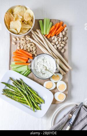 Homemade herby whipped feta dip on an aperitif platter with chips, raw vegetables, nuts, grissini sticks, asparagus and boiled eggs Stock Photo