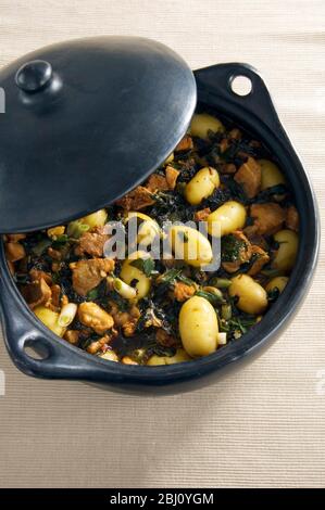 Black earthenware casserole with dish of pork spinach and potatoes with soy sauce - Stock Photo