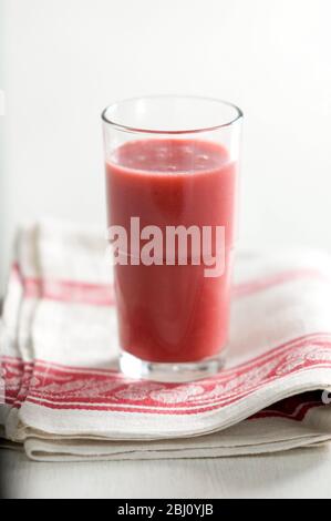 Glass of red raspberry smoothie on vintage red and cream cloth - Stock Photo