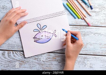 Female hands drawing whale in notebook on wooden table background Stock Photo