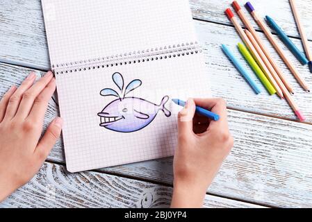 Female hands drawing whale in notebook on wooden table background Stock Photo