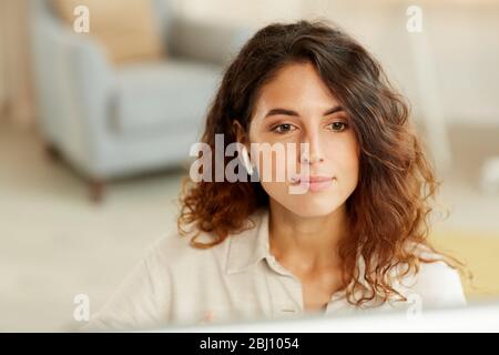 Horizontal medium close-up portrait of young adult Caucasian businesswoman working on computer at home Stock Photo