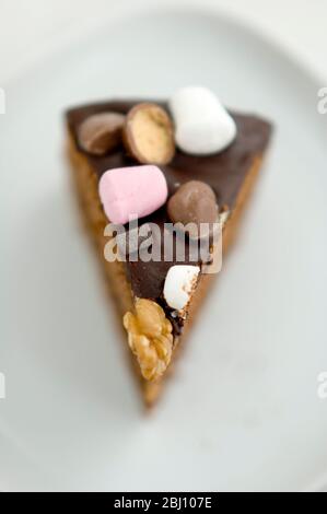 Slice of chocolate 'Rocky Road' cake topped with nuts, marshmalllows and candies - Stock Photo