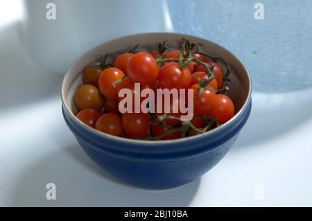 Small cherry tomatoes on the vine in a blue ceramic bowl - Stock Photo
