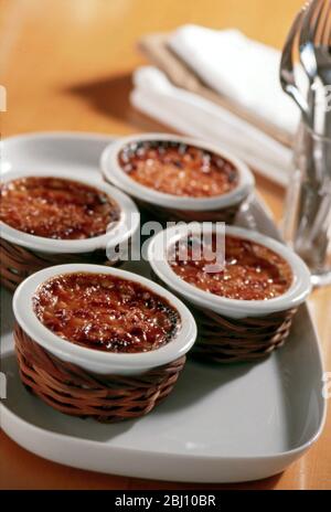 Four classic creme brulees in white ramekins in baskets - Stock Photo