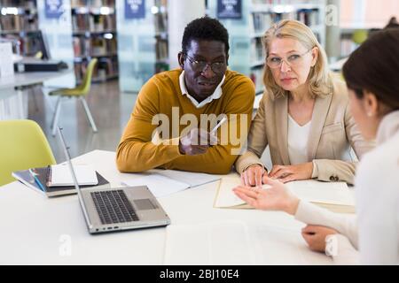 Female tutor helping students preparing for exam in library Stock Photo