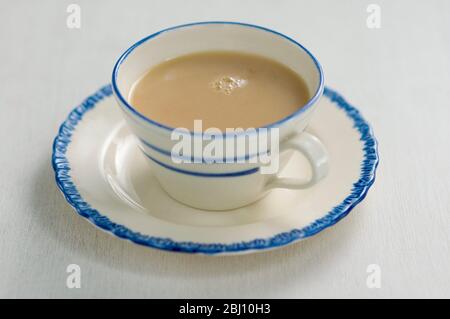 Blue and cream china cup and saucer with milky tea. - Stock Photo