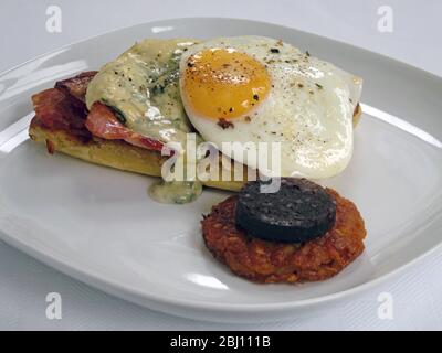 Full English breakfast of bacon & egg with melted gruyere on toast - plus black pudding and hash browns - Stock Photo