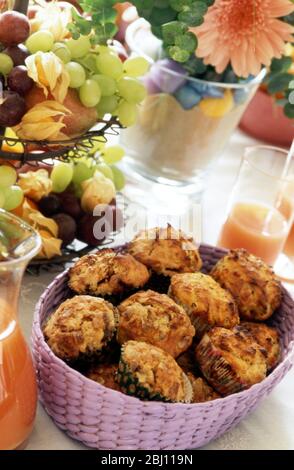 Brunch table set out with basket of bacon muffins with pink grapefruit juice and bowl of fresh fruit - Stock Photo