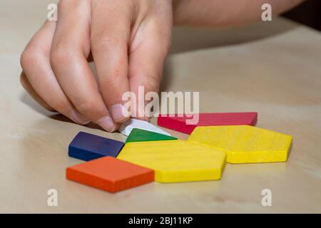 Tangram geometric colored shapes puzzle piece with hand filling in pieces on brown background. Stock Photo
