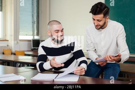 Two male university students sitting at desk discussing their student project Stock Photo