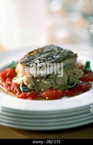Piece of pan-fried cod on bed of butter beans and tomatoes with coriander on stack of plates -