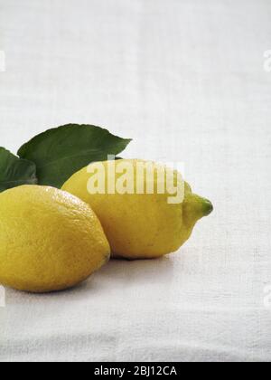 Two whole lemons on white linen cloth with lemon leaves - Stock Photo