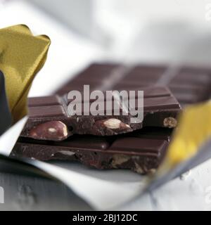 Chocolate almond nut bar broken and sitting on wrapping - Stock Photo