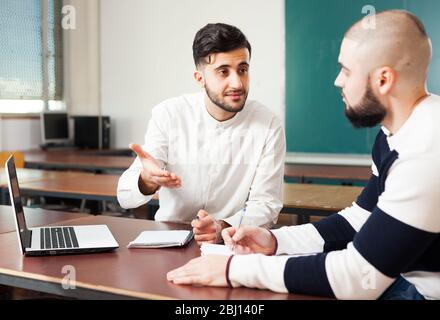 Portrait of two young guys working on their student project at desk in classroom Stock Photo