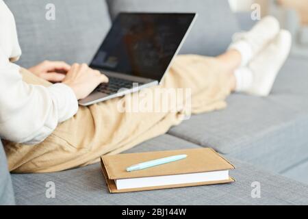 Unrecognizable woman sitting relaxed on sofa at home working on her laptop, horizontal shot Stock Photo