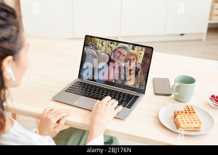 Unrecognizable young woman getting video call from her parents on laptop, sitting at desk at home Stock Photo