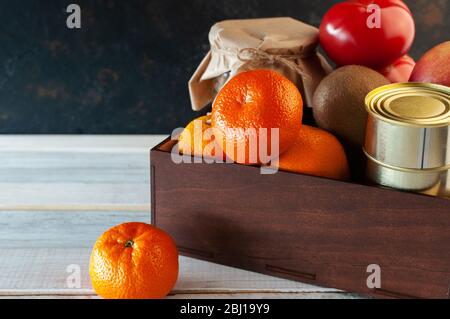 Food delivery during quarantine and isolation. Products folded in a box on a wooden white table background. Fruits vegetables, canned goods, cereals Stock Photo