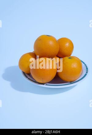 Many vitamin C-rich oranges are placed in a ceramic dish on a white background. Stock Photo