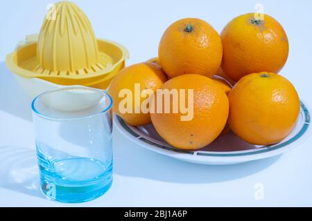An empty glass with a juicer on the side and a plate full of vitamin C-rich oranges are photographed above a white background. Stock Photo
