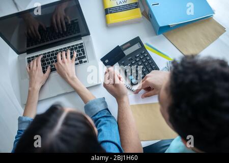 Female hands typing on laptop, male hands holding credit card Stock Photo