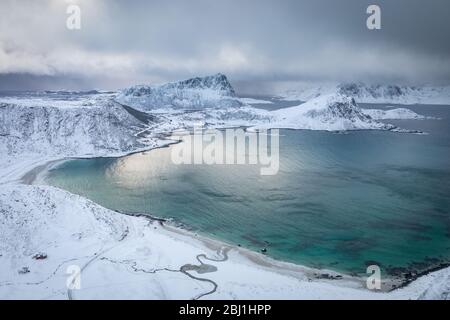 View from Mannen mouintain at Haukland beach in winter before snow storm. Blue, clean sea and snow covered mountains under grey, stormy clouds. View f Stock Photo