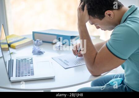 Dark-haired male sitting at his desk, filling in unemployment claim Stock Photo
