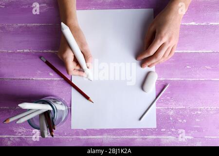 Hand with color pencils and blank sheet of paper on wooden table Stock Photo