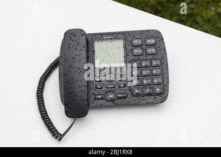 Black stationary desktop touch tone telephone on white table outdoor covered with waterdrors. Remote workplace, communication, online work office. Bas Stock Photo