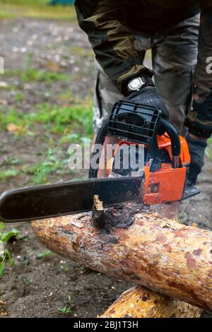 Close up hands of man holding chainsaw, sawdust fly to sides Stock Photo