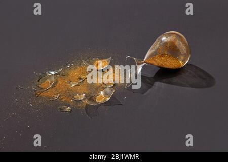 Broken antique hourglass with golden sand on a black background. Stock Photo