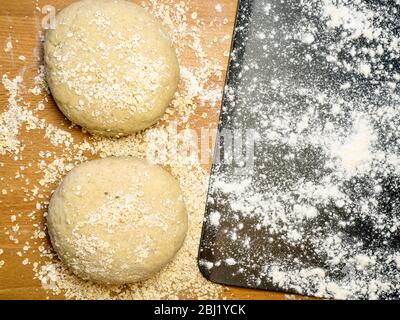Two rounds of oat bread dough rolled in oats with a floured baking sheet on a kitchen table Stock Photo