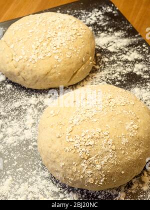 Two rounds of oat bread dough rolled in oats on a floured baking sheet on a kitchen table Stock Photo
