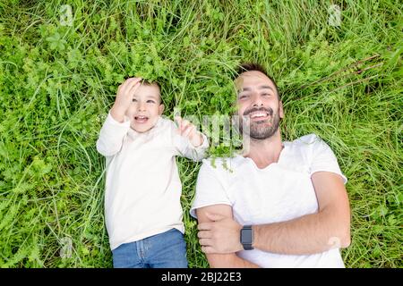 High angle view of smiling bearded man and young boy lying in grass. Stock Photo