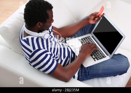 African American man with laptop and credit card on sofa Stock Photo