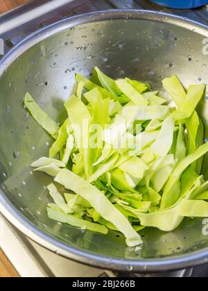 Washed fresh pointed cabbage slices in a stainless steel colander on a kitchen drainer Stock Photo