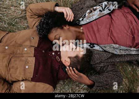 Overhead view of a black woman and white man on the ground, heads together, kissing. Stock Photo