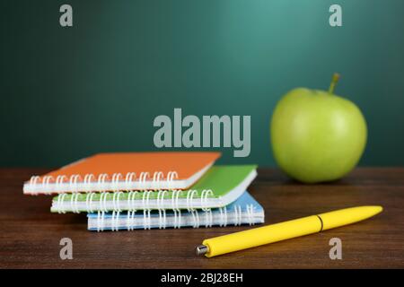 Colorful notebooks with pen and green apple on desk on green chalkboard background Stock Photo