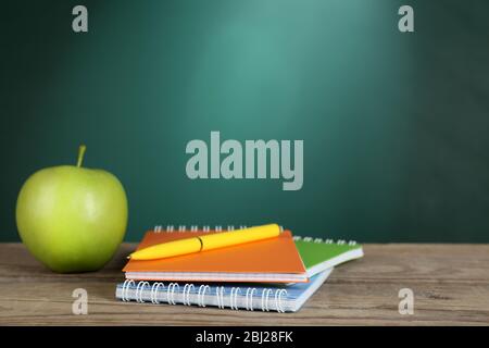 Green apple, colorful notebooks and pen on desk on green chalkboard background Stock Photo