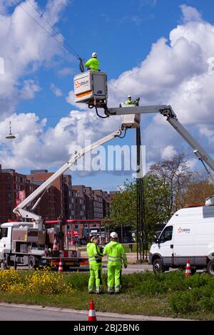 Lineworkers working on power lines in crane buckets high in the air from aerial lift and other workers watching from the ground. Copenhagen, Denmark - Stock Photo