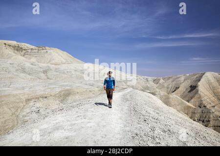 Tourist in hat walking at the trail on surreal white mountains against blue sky in desert park Altyn Emel in Kazakhstan Stock Photo