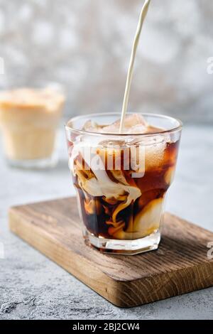 Pouring cream in iced coffee in rocks glass Stock Photo