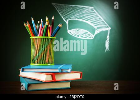 Metal cap of crayons, stack pf books and bachelor hat drawing on blackboard background Stock Photo